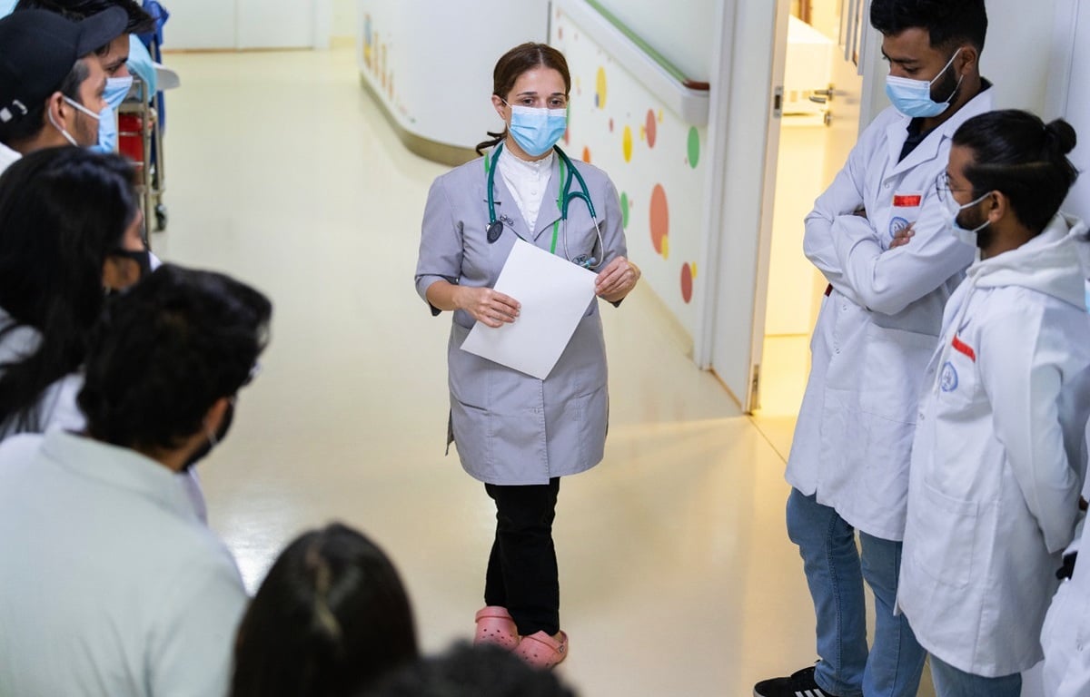 A woman doctor is briefing her colleagues in a corridor at a hospital.